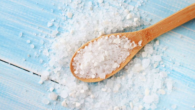 Coarse grain sea salt on a wooden spoon and scattered on a blue wooden table