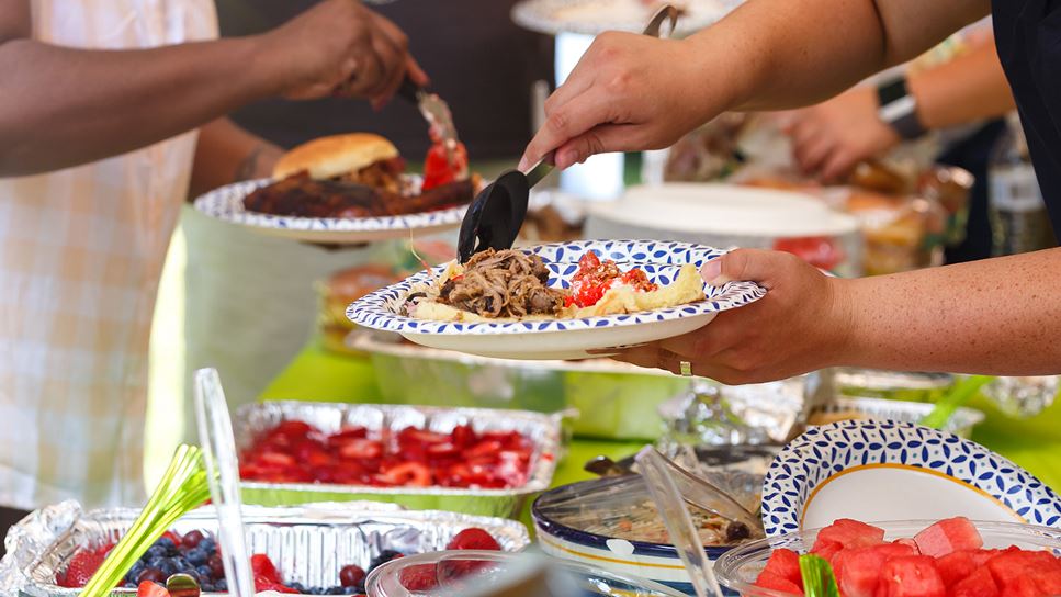 A buffet table with multiple hands scooping food from the variety of dishes. 
