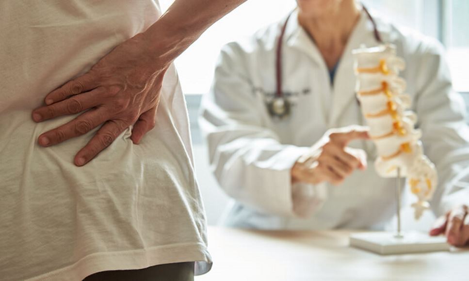 person holding their lower back and doctor with spine model demonstrating bone health