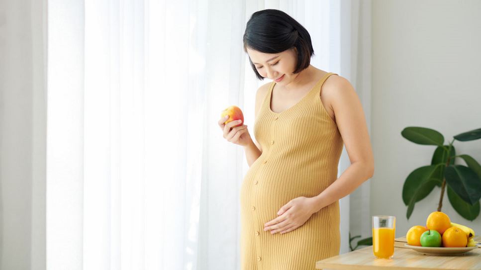 Pregnant woman holding belly with one hand and a glass of juice with the other
